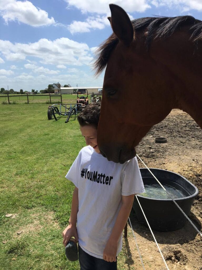 Made in the Stars, a Heart Horse Story, Scout a Dutch Warmblood gelding, with muzzle up to boy's face. Boy wearing a white YouMatter tshirt